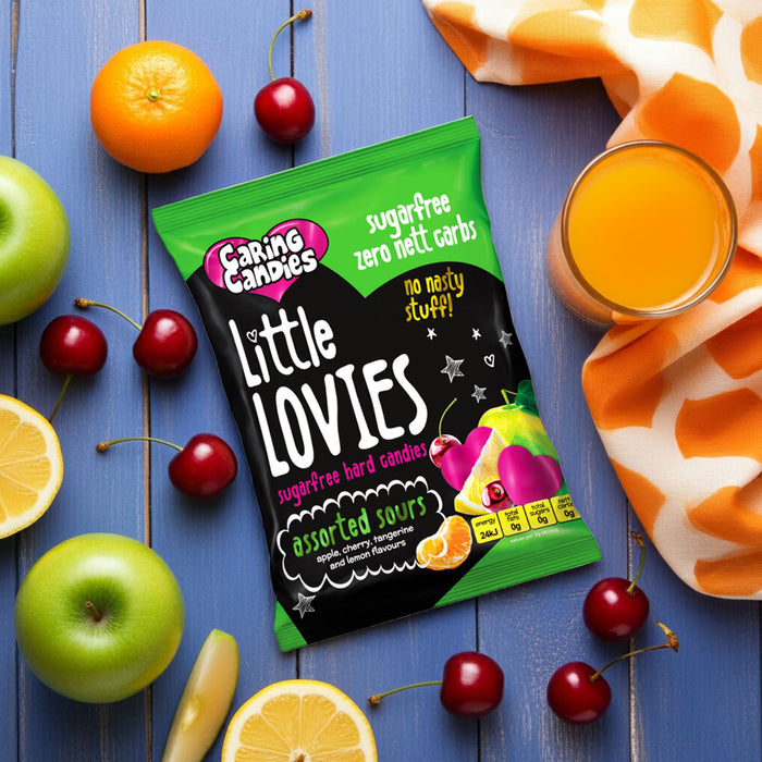 Packaging of Caring Candies sugarfree Little Lovies sweets on a blue wooden surface with fruits and juice.