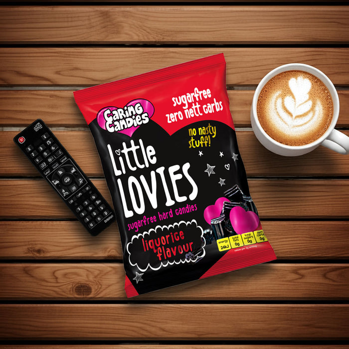 Pack of sugarfree caring candies Little Lovies liquorice flavoured sweets on a wooden surface with a cup of coffee and remote control.