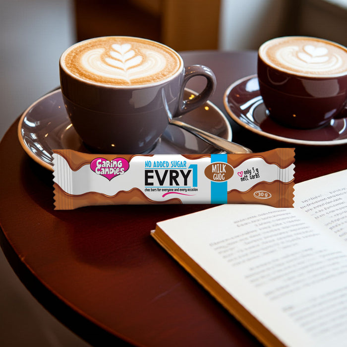 Two cups of coffee with a bar of EVRY1 sugar-free milk chocolate on a table next to an open book.