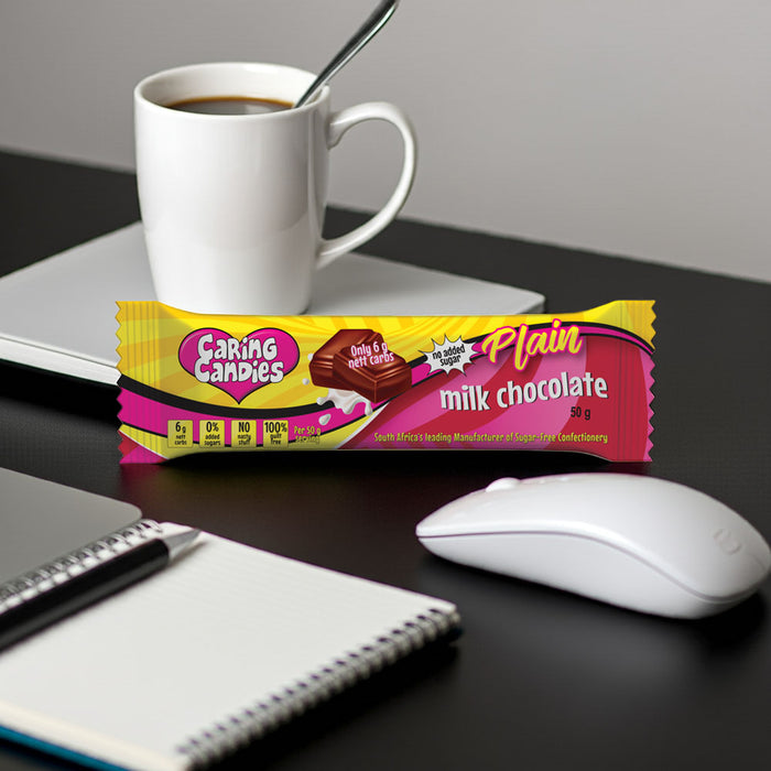 Caring Candies plain milk sugar-free chocolate bar on a desk with a cup of coffee, mouse, and notebook.