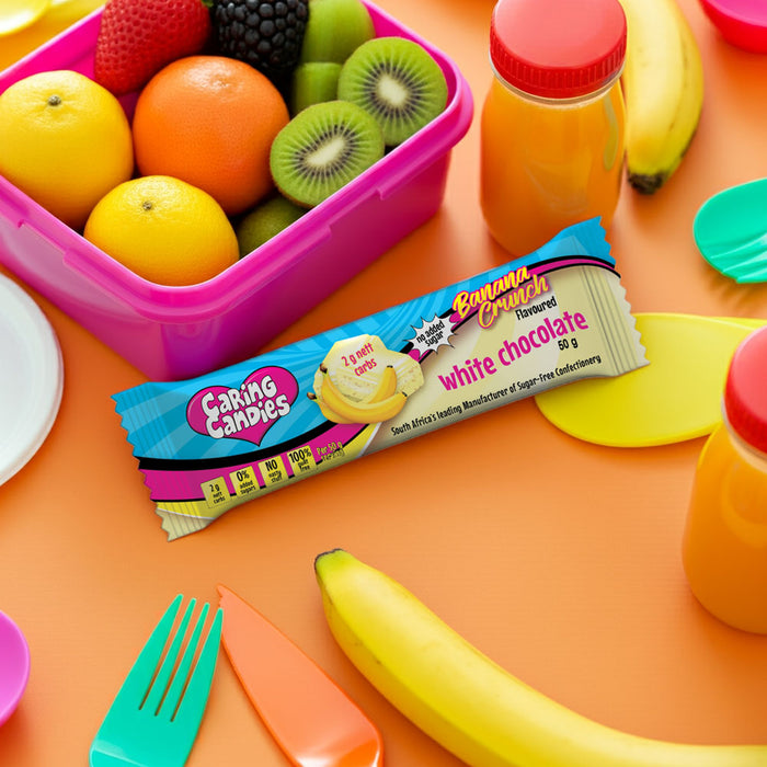 Banana Crunch white chocolate caring candies bar with a fruit container and juice bottles on an orange background