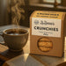 ZuZanna's Sugarfree Crunchies packaging with a steaming cup of coffee on a wooden surface.