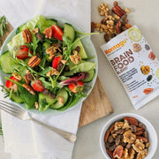 Salad with strawberries, cucumbers, and nuts on a plate next to a package of Montagu Brain Food Blend.