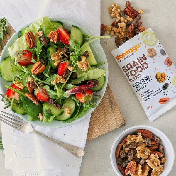 Salad with strawberries, cucumbers, and nuts on a plate next to a package of Montagu Brain Food Blend.