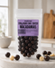 Packaged  no added sugar dark chocolate-coated macadamias with a purple label on a marble surface.