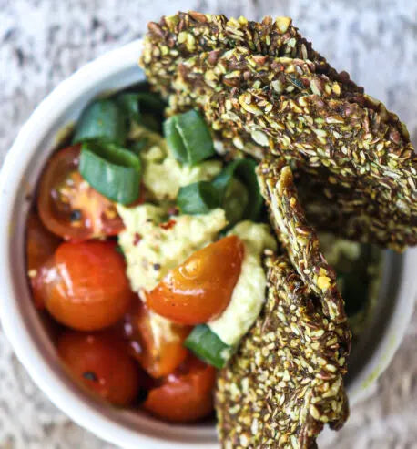 Bowl of salad with cherry tomatoes and green onions, topped with a spicy pumpkin cracker.