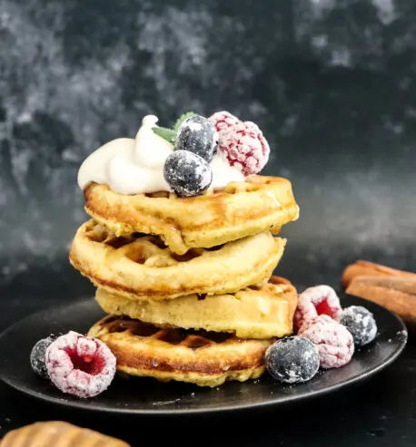 Stack of waffles with berries and whipped cream on a dark background