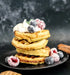 Stack of waffles with berries and whipped cream on a dark background