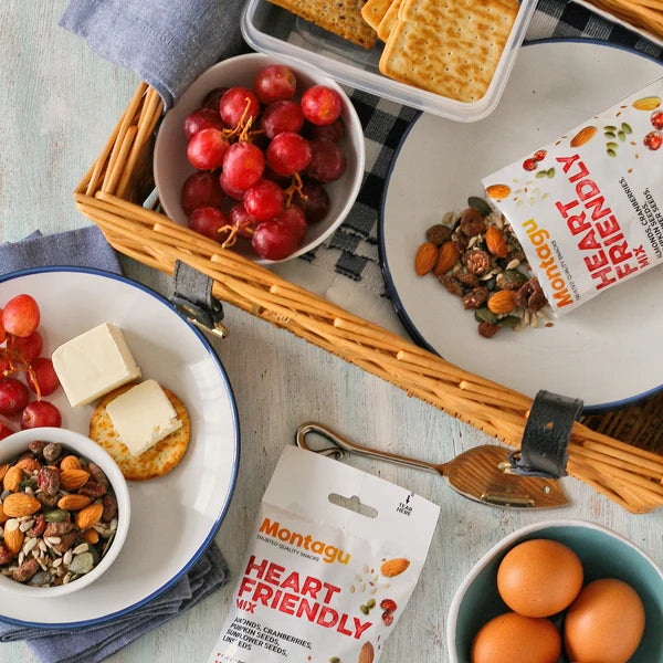 Assorted snacks including grapes, crackers, and Montagu Heart Friendly snack bars on a picnic blanket.