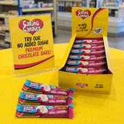 Caring Candies chocolate bars with packaging and promotional signs on a yellow surface.