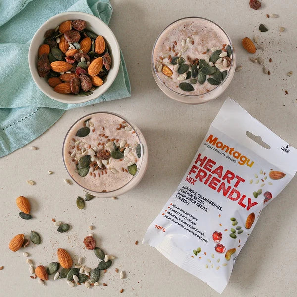 Two bowls of a smoothie with nuts and seeds, a package of Montagu Heart Friendly snack mix, and a bowl of mixed nuts on a light surface.