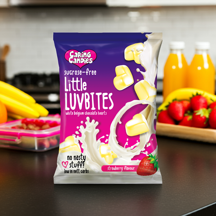 Packaging of Caring Candies Little LUVBITES on a kitchen counter with fruits and juice in the background.