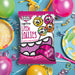 Caring Candies sugarfree Little Lollies packet with colorful party supplies on a blue background
