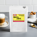 White package of sugar-free erythritol with a yellow label on a gray surface, coffee cup and cookies in the background.